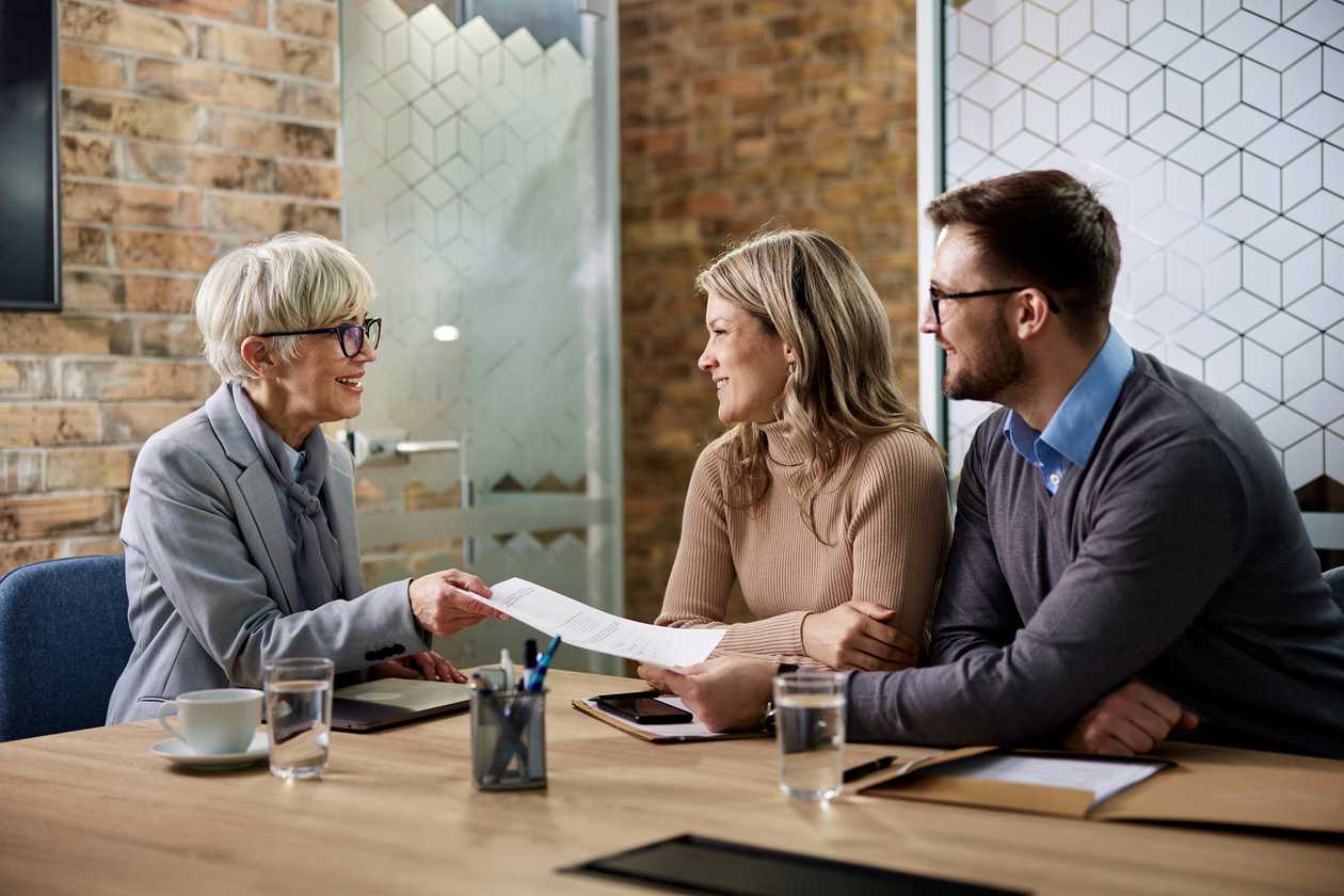 An adviser handing a document to a couple across a meeting-room table